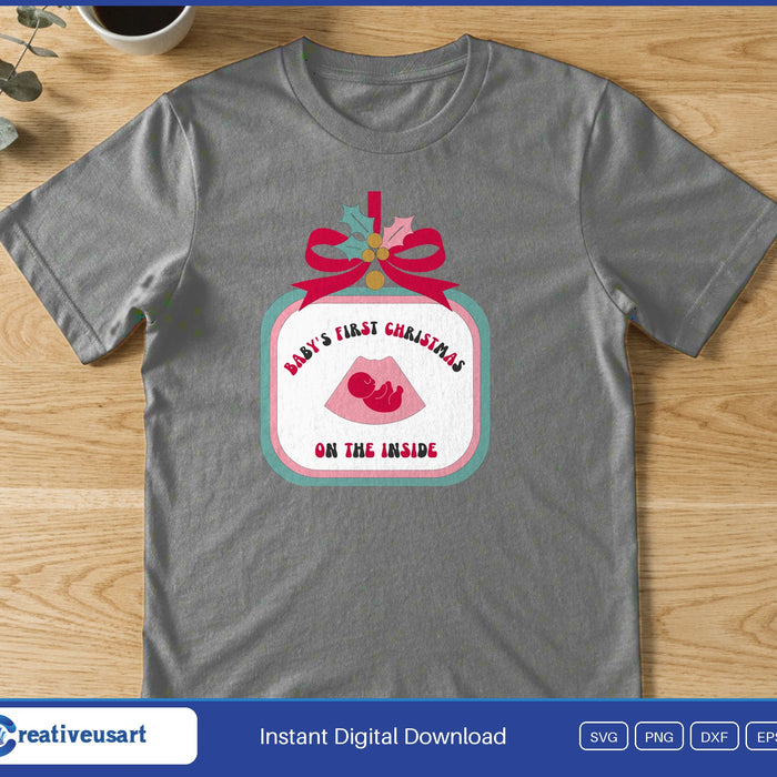 An ornament with a pink bow holding a baby ultrasound, with the words Baby's First Christmas On The Inside, on a gray t-shirt