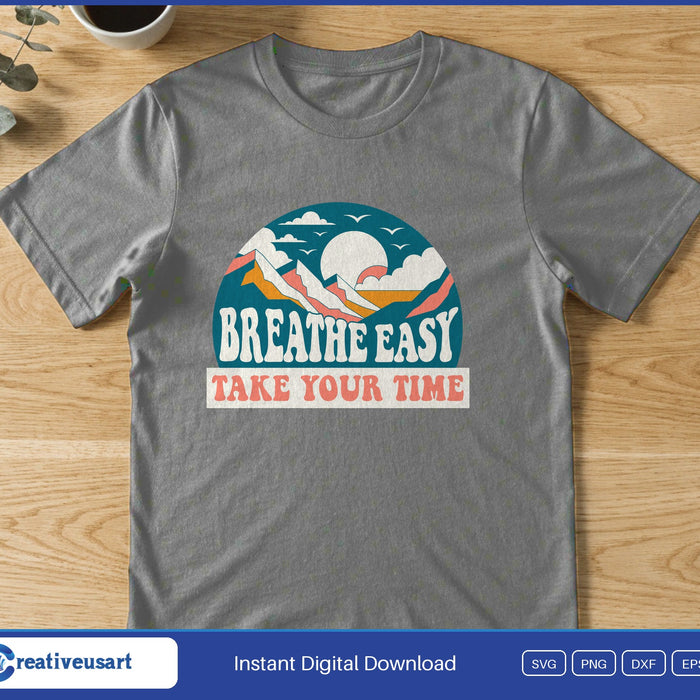 A retro badge with a sunrise over mountains and the words Breathe Easy Take Your Time, on a gray t-shirt
