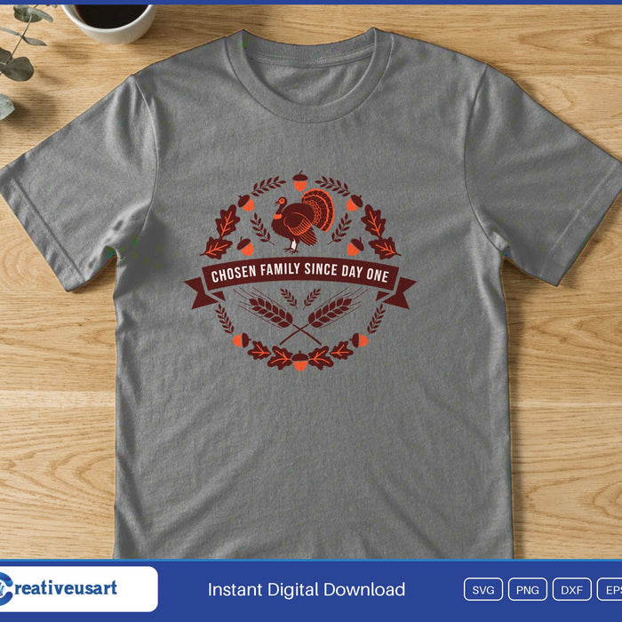 A turkey inside a round wreath of leaves and wheat with a banner reading Chosen Family Since Day One, on a gray t-shirt