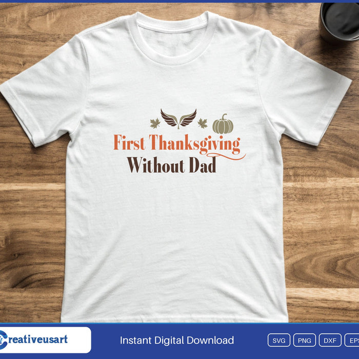 Script lettering reading First Thanksgiving Without Dad below small angel wings and a pumpkin, on a white t-shirt