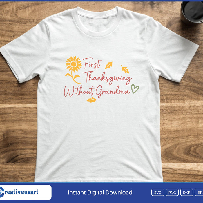 Script lettering reading First Thanksgiving Without Grandma with a sunflower, falling leaves and a heart, on a white t-shirt
