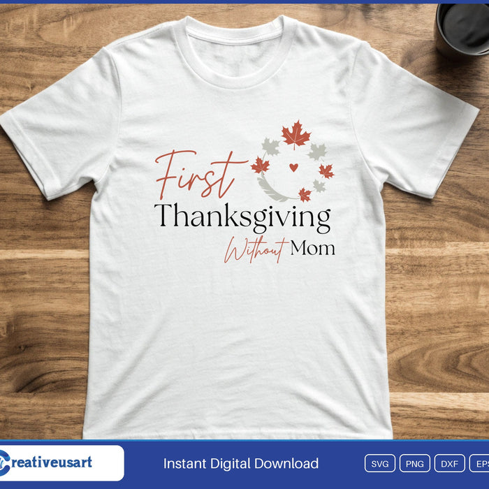The words First Thanksgiving Without Mom inside a partial wreath of autumn leaves, on a white t-shirt