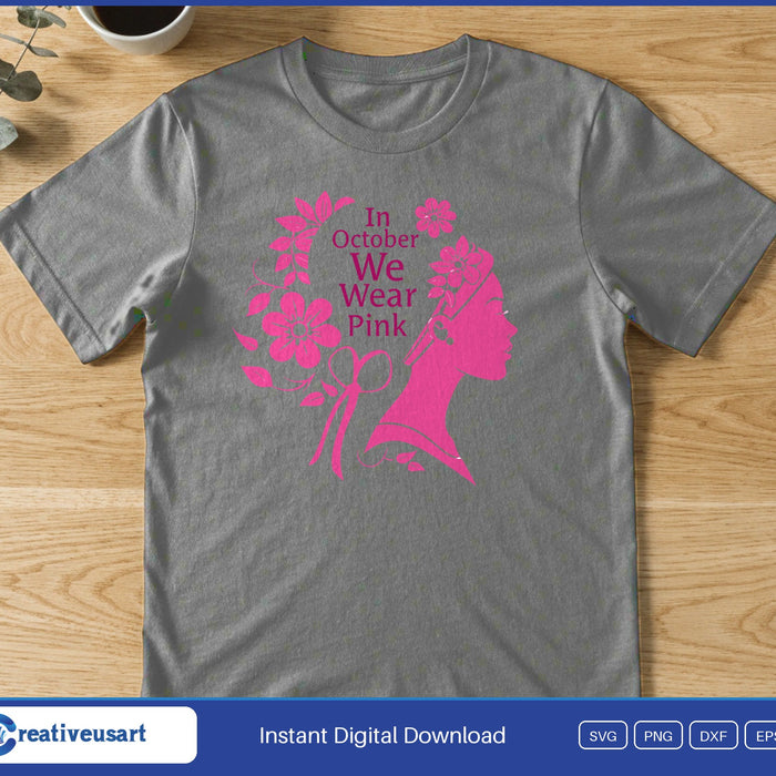 A woman's profile in pink with flowers in her hair and a ribbon, beside the words In October We Wear Pink, on a gray t-shirt