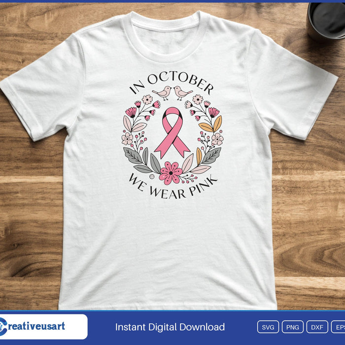 A pink ribbon inside a folk style flower wreath, ringed by the words In October We Wear Pink, on a white t-shirt
