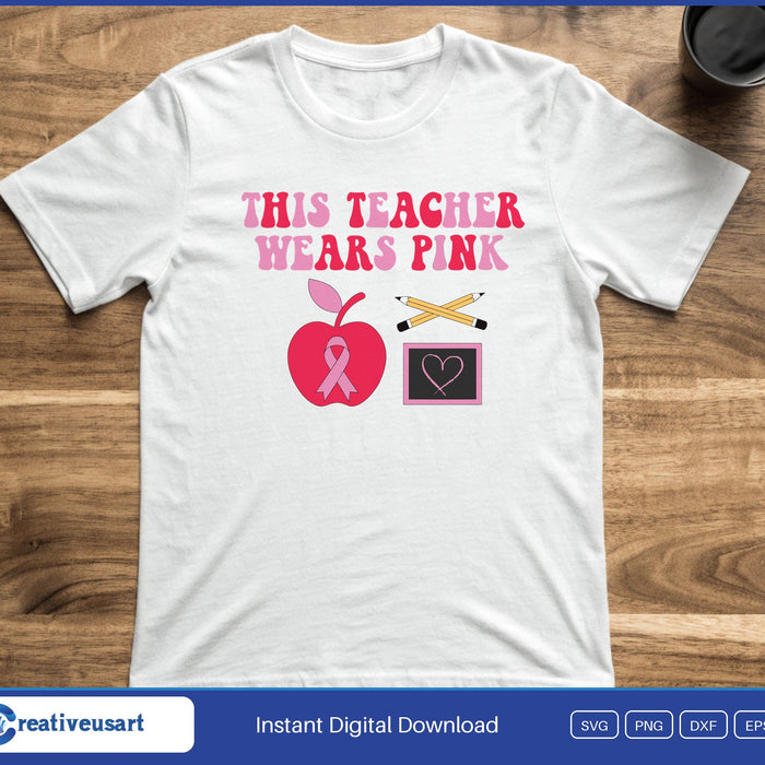 The words This Teacher Wears Pink above an apple with a pink ribbon, two pencils and a small chalkboard heart, on a white t-shirt